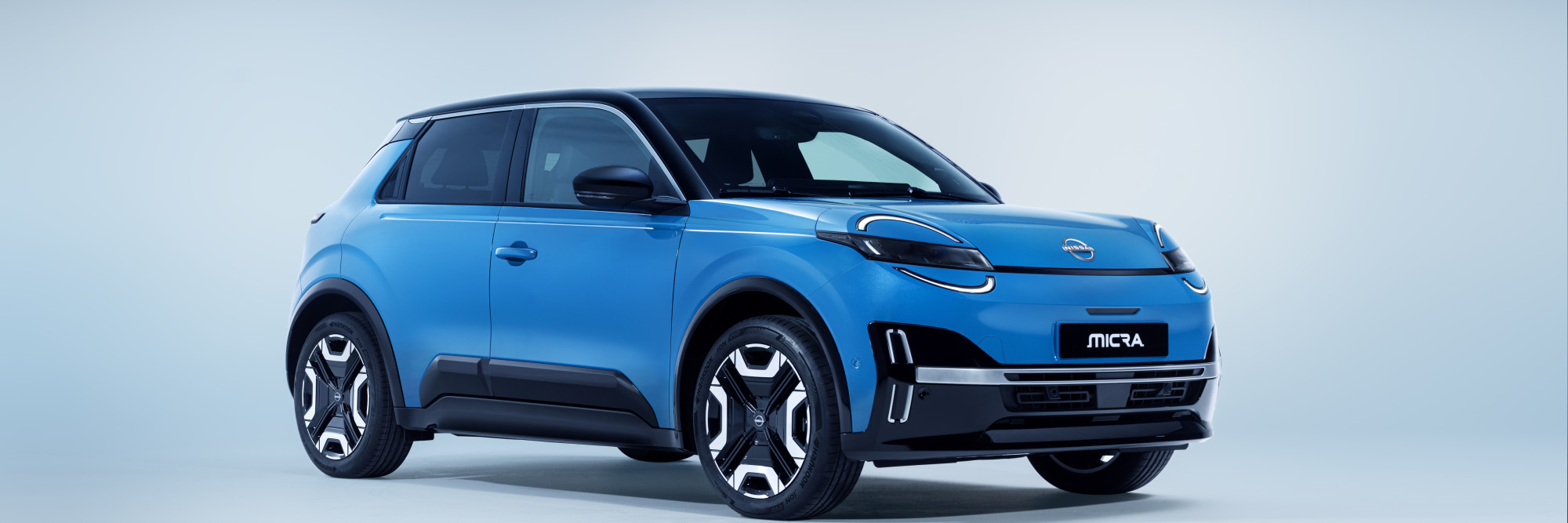 4 view of new Micra in gear blue body color, black roof, wheels. signature headlamps, Micra & Nissan nameplate