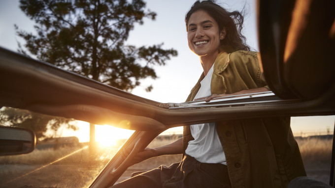 Happy young woman hanging out of the car window